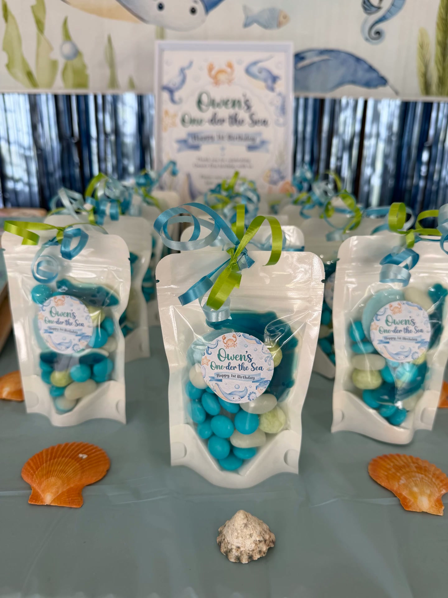 White favour bags with blue lollies and personalised 'Owen's One-der the Sea' birthday labels tied with ribbon