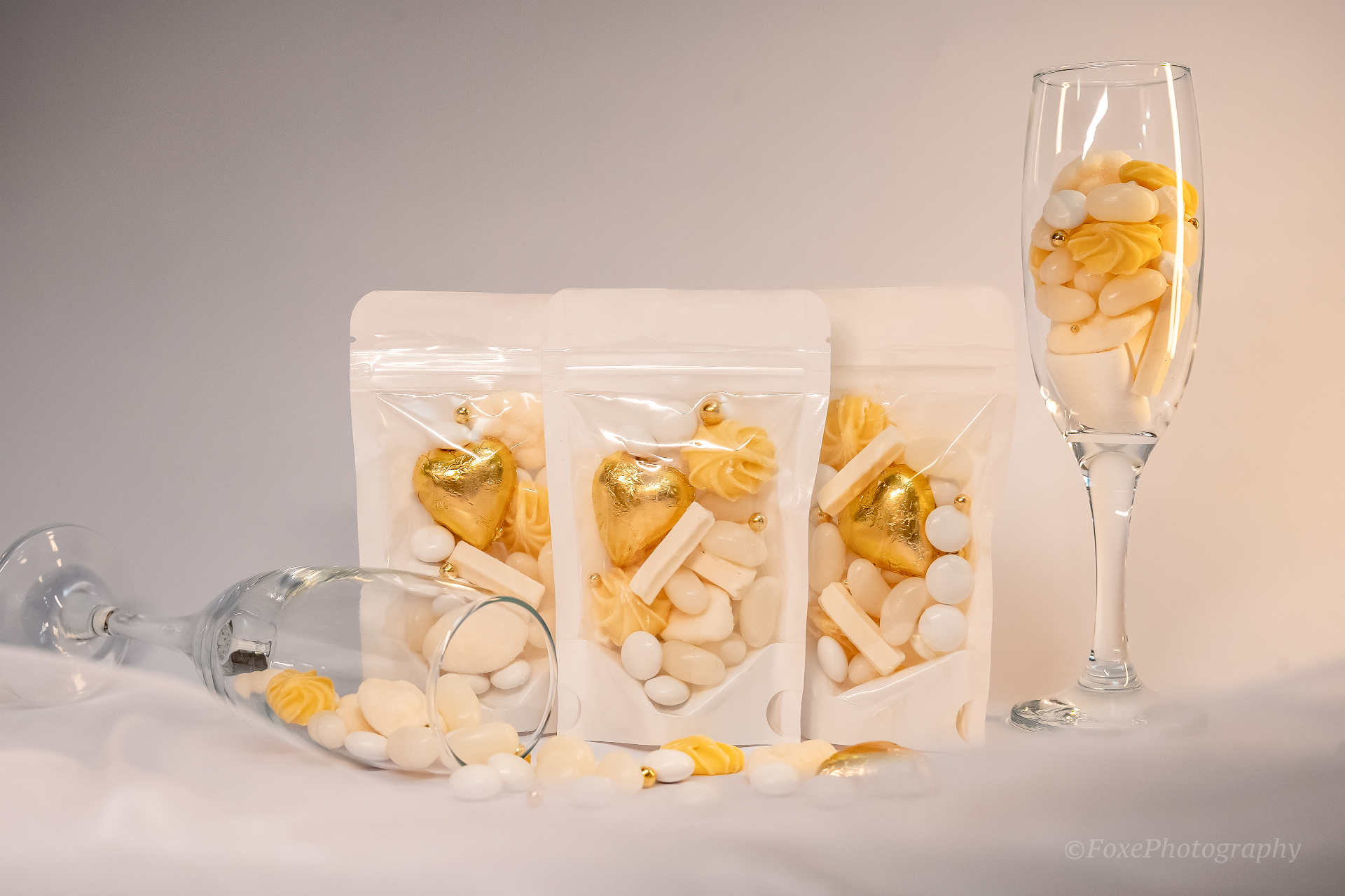Trio of white and gold party favour bags filled with jelly beans, meringues, gold foil hearts and champagne glasses