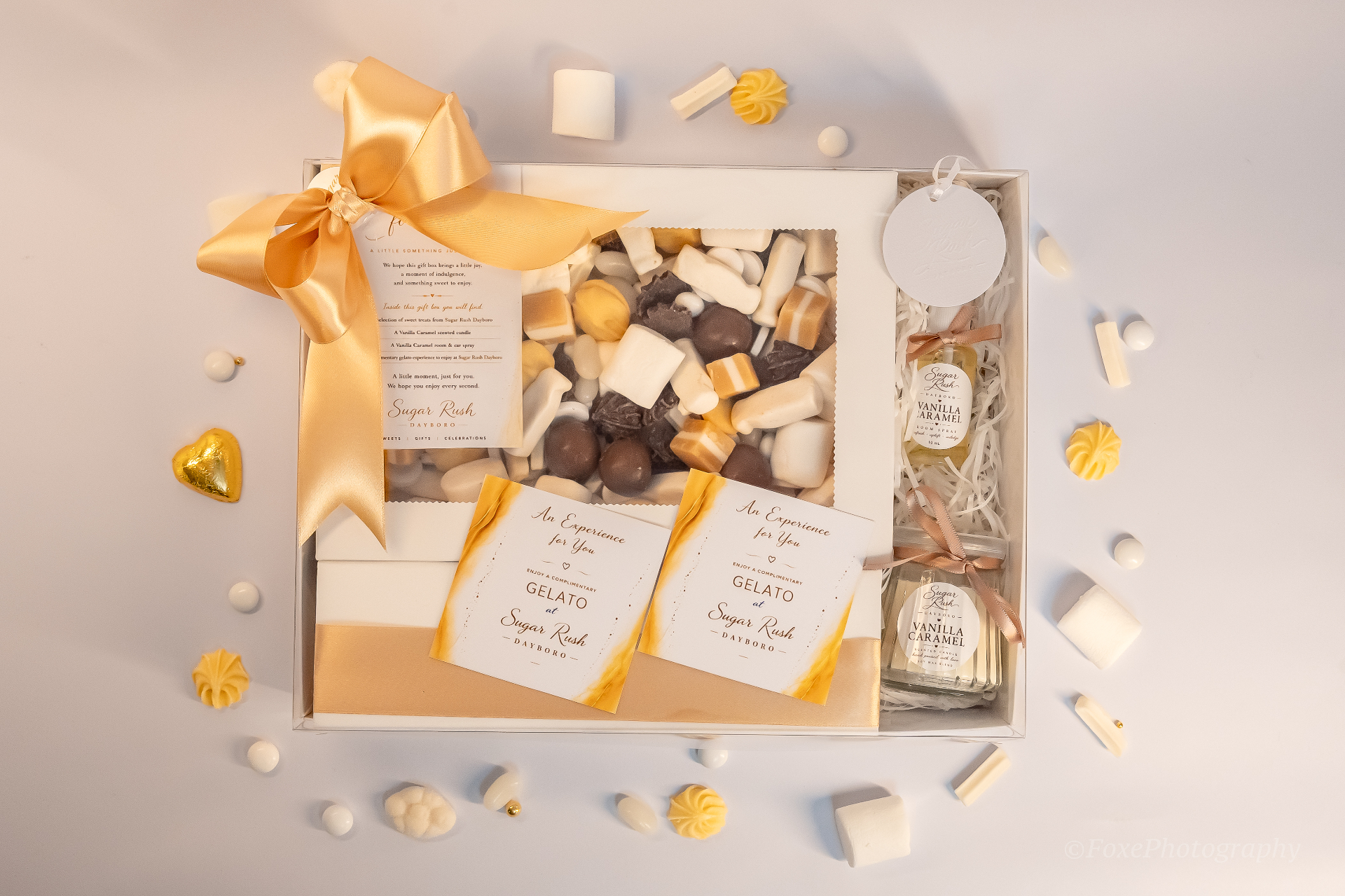 Elegant white and gold corporate gift box with gold satin bow, assorted chocolates, vanilla caramel candle and room spray, plus complimentary gelato vouchers